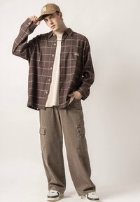 Hnedo-krémová košeľa s károvaným vzorom na gombíky v kombinácii s béžovými cargo nohavicami. Doplnok tvorí čiapka a tenisky, čím vzniká pohodlný, vrstvený vzhľad.