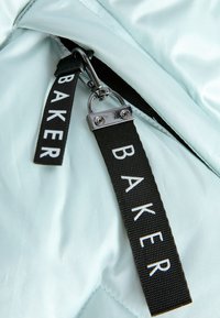 Svijetloplava nabrana tkanina ima srebrni patentni zatvarač s crnom trakom za povlačenje na kojoj je natpis "BAKER" u bijeloj boji. Glatka tekstura s sjajem.