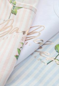 Morceaux de tissu pliés à rayures pastel avec des imprimés floraux et un texte en cursive dorée brillante, délicatement superposés sur une surface claire.