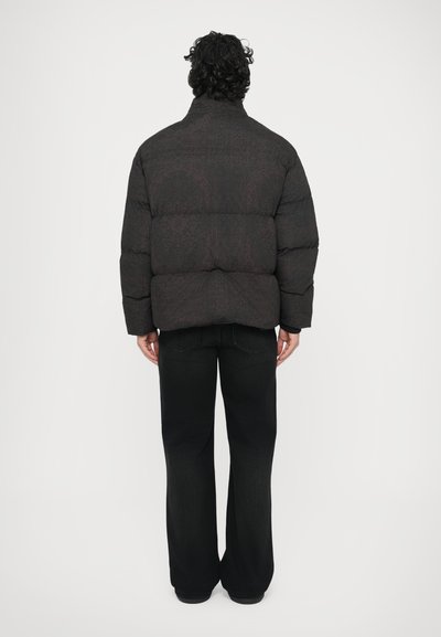 Sort dunjakke med quiltet tekstur, høj krave og diskret mønster; kombineret med løse sorte jeans og flade sko.