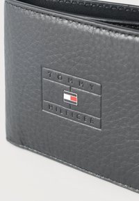 Μαύρο πορτοφόλι από δέρμα με υφή, με ανάγλυφο λογότυπο Tommy Hilfiger και μικρή ορθογώνια σημαία σε κόκκινο, λευκό και ναυτικό μπλε στην πρόσοψη.