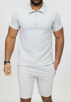 Polo shirt gris clair à manches courtes avec col zippé et motif en relief. Associé à un short assorti avec poches zippées sur les côtés.