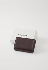 Calvin Klein wallet in burgundy with textured finish and diagonal logo pattern; packaged in a white branded box.