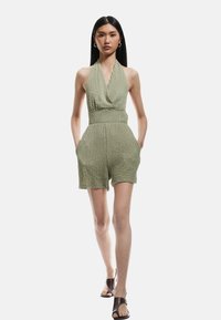 Olijfgroene halterneck romper van textuurstof, met een aansluitende taille en zijzakken. Heeft een ontspannen pasvorm en een lengte boven de knie.