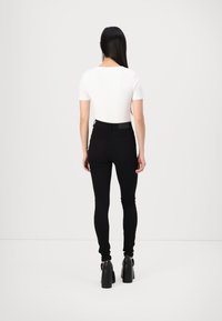 Zwarte high-waisted jeans met een gladde textuur, gecombineerd met een aansluitend wit T-shirt met korte mouwen. Zwarte plateauhakken maken de outfit compleet.