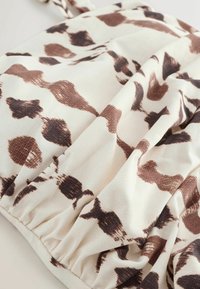 Tissu beige avec des taches brunes abstraites et des lignes ondulées, rassemblé sur le bord inférieur, ressemblant à un motif d'imprimé animal.