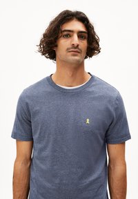 T-shirt blu a maniche corte in tessuto mélange con scollatura rotonda e piccolo logo a nastro giallo sul petto.
