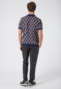 Kurzärmliges Strick-Polo-Shirt mit einem geometrischen Muster in Marineblau, Burgunderrot und Grau, mit geripptem Kragen und Bündchen. Kombiniert mit dunklen Hosen.