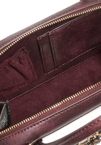 Burgundy leather handbag interior featuring smooth texture, zip closure, and multiple card slots. Gold zipper detail along the edge.