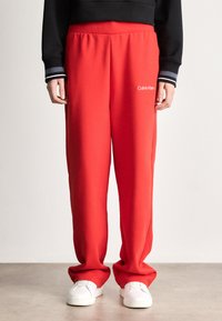 Czerwone dresy w luźnym kroju, z elastycznym paskiem, z logotypem Calvin Klein z przodu. Zestawione z białymi trampkami i czarną bluzką.