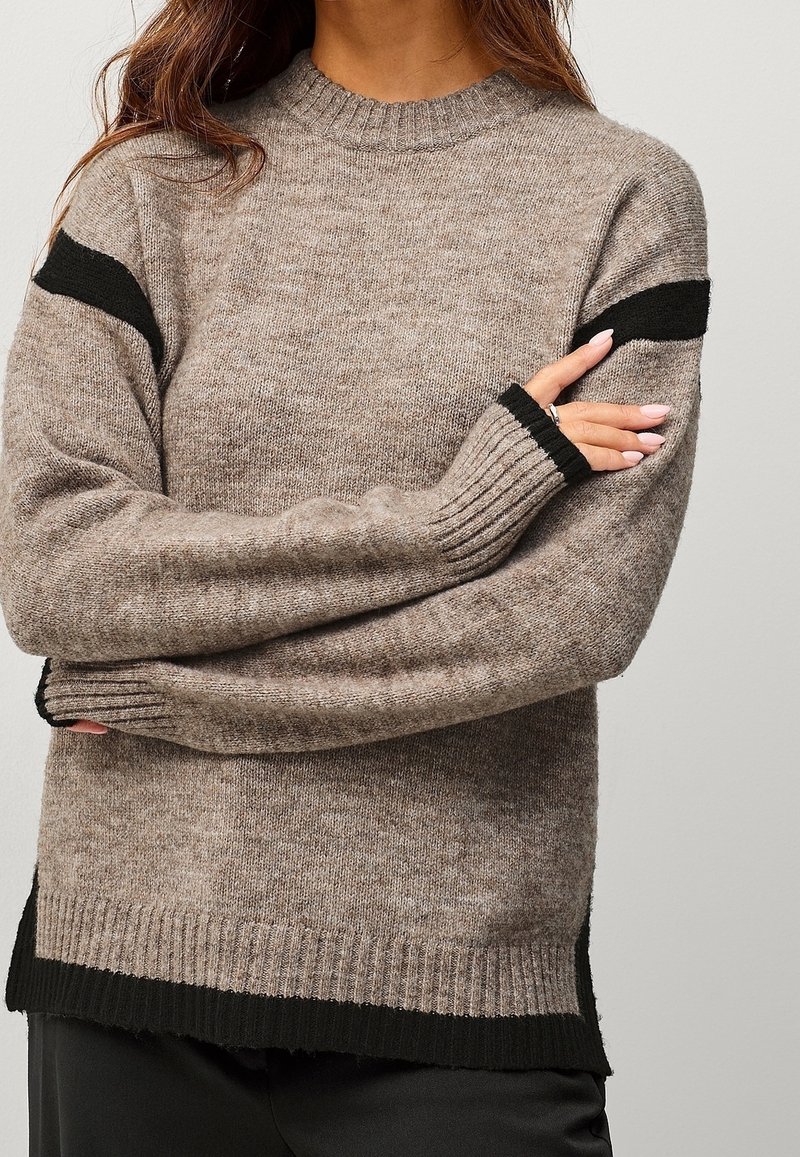 Pull en maille marron avec des rayures noires sur les épaules, des poignets et un ourlet côtelés. La texture semble douce et confortable.