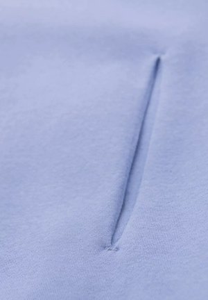 Jasnoniebieska tkanina o gładkiej fakturze ma pionowy szew na środku, tworząc dyskretną kieszeń lub szczegół otwarcia.