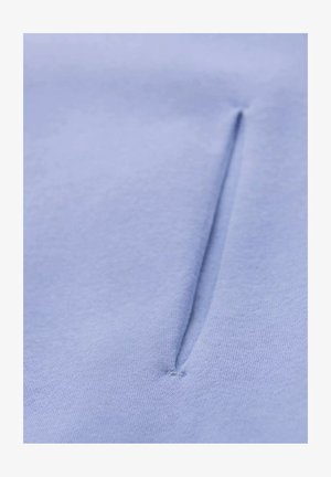 Světlomodrá látka s hladkým povrchem má uprostřed svislý šev, který vytváří nenápadnou kapsu nebo otvor.