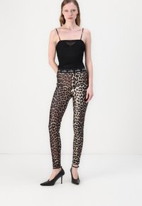 Leggings s uzorkom leoparda i crnim pojasom, u kombinaciji s prilagođenim crnim majicom. Materijal ima glatku teksturu s sjajnim finishem.