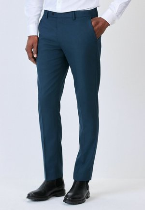 Dunkelblaue Stoffhose aus glattem Material, mit schmaler Passform, seitlichen Taschen und flacher Vorderseite, getragen mit schwarzen Stiefeletten.