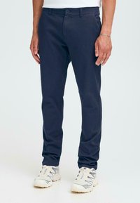 Marineblå slim-fit chinos laget av vevd stoff. Har frontlommer, beltehemper og en knapplukking. Brukt med hvite joggesko.