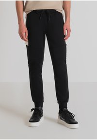 Zwarte joggingbroek met een trekkoord in de taille, voorzien van textuurpanelen. Gecombineerd met zwart-witte sneakers.