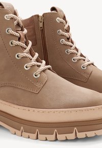 Stivaletti alla caviglia in pelle tan con finitura testurizzata, dotati di lacci crema, una zip laterale e una suola spessa beige con motivo rigato.