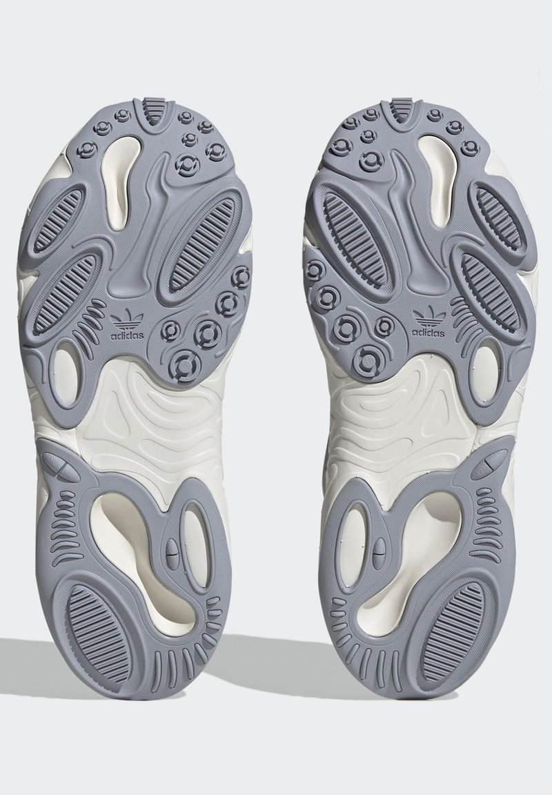 Weiße und graue Sohlen von Sport Schuhen mit strukturiertem Gummi, der einzigartige Konturen, Rillen und kreisförmige Griffe aufweist, um die Traktion zu verbessern.