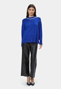 Maglione blu a maglia con scollo rotondo e colletto arricchito, abbinato a pantaloni larghi neri in ecopelle e décolleté a punta.