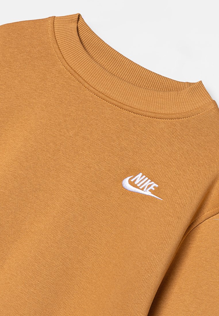 Sweatshirt jaune moutarde avec un col ras du cou côtelé et un petit logo Nike blanc sur la poitrine gauche. Texture de tissu lisse.