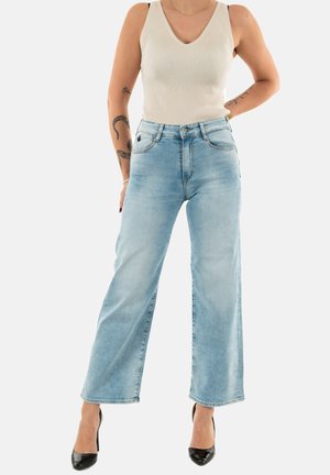 Light blue high-waisted wide-leg jeans with five pockets, metal button, and zip fly. Ribbed white tank top with a V-neck design. Classic black heels.