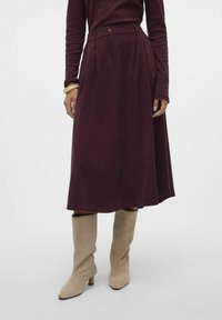 Burgundin, polven mittainen hame, jossa on poimutuksia, valmistettu pehmeästä kankaasta. Yhdistetty taipuvan näköisiin, kermavärisiin, polven yli ulottuviin saappaisiin, joissa on kapea kärki.