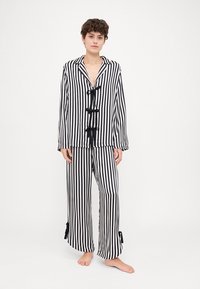 Black and white striped pajama set featuring a loose button-up top with ties and wide-leg pants with slits at the hem.