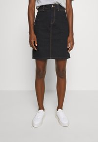 Gonna di jeans scuri con taglio dritto, chiusura con bottoni frontali e cuciture a contrasto. Abbinata a sneakers bianche per un look casual.