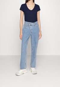 Marineblaues kurzärmeliges V-Ausschnitt-Oberteil kombiniert mit hellblauen geraden Jeans und weißen Sneakern, mit einer lässigen Passform und klassischem Denim-Design.
