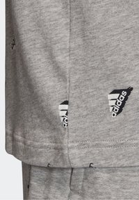 Szary bawełnowy T-shirt z czarnym nadrukiem logo Adidas, okrągłym dekoltem i krótkimi rękawami. Szczegółowe przeszycia na dolnym brzegu.