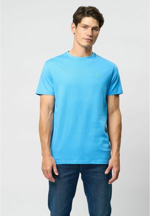 Lichtblauw katoenen t-shirt met korte mouwen, ronde hals en een klein groen logo op de linkerkant van de borst. Draagt met donkerblauwe jeans.
