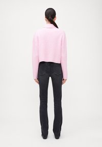 Pulover scurt roz cu dungi, cu mâneci lungi, asortat cu blugi negri ajustați, având un design clasic cu cinci buzunare.