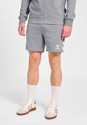 Mand iført grå sportsshorts med hummel-logo, matchende grå lynlåstrøje, hvide ankelsokker og hvide sneakers med gummisåler.