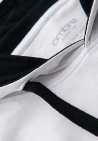 Detailní záběr na bílou mikinu s černou šňůrkou a viditelným vnitřním štítkem s nápisem "ambre cotton, 100% čistá bavlna."