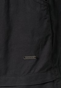 Chaqueta de tela negra con un acabado texturizado. Cuenta con una pequeña etiqueta metálica con la marca "ROXY". Incluye bolsillos y un acabado de costura limpio.