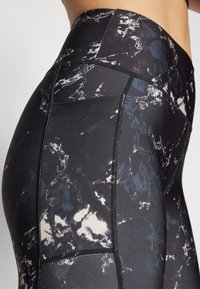 High-waisted leggings in a black and navy abstract print, featuring a smooth texture, contrasting stitching, and a side pocket.