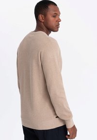Beige Strickpullover mit strukturiertem Finish, runder Ausschnitt und langen Ärmeln. Figurbetonte Passform mit einem dezenten Logoakzent am Saum.