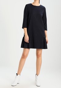 Marineblaue, knielange Kleid mit vertikalen weißen Streifen, rundem Ausschnitt und 3/4-Ärmeln; ausgestellter Rock mit subtilen Falten.