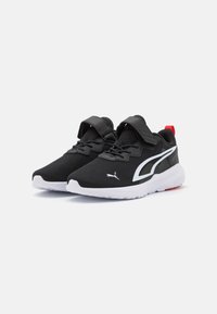 Scarpe da ginnastica nere con una parte superiore in tessuto, accenti bianchi, una cinghia e lacci, e una suola in gomma, con un tab di tacco rosso e logo.