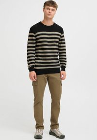 Black striped sweater with cream and gold horizontal lines. Paired with khaki cargo pants and gray footwear. Simple, casual design.