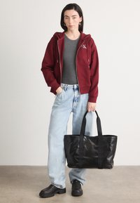 Bordo zip-up dukserica, siva majica ispod, svijetli traperice, crna kožna torba s ručkama i crne chunky cipele.