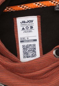 Oranje en zwart gestreepte stof met een geweven oranje en zwarte accent. Bevat een label met een QR-code, merknaam en onderhoudsinstructies.