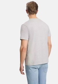 Szara koszulka z krótkim rękawem, wykonana z miękkiego materiału, o prostym kroju i okrągłym dekolcie, noszona z jasnoniebieskimi dżinsami.