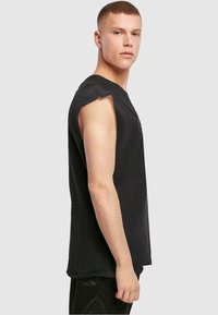 Sort ærmeløs T-shirt lavet af bomuld, med rund hals og råskårede ærmegab. Enkelt design med minimal dekoration.