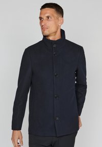 Abrigo de mezcla de lana azul marino con cuello alto, seis botones negros y bolsillos laterales. Textura suave, corte entallado y diseño estructurado.