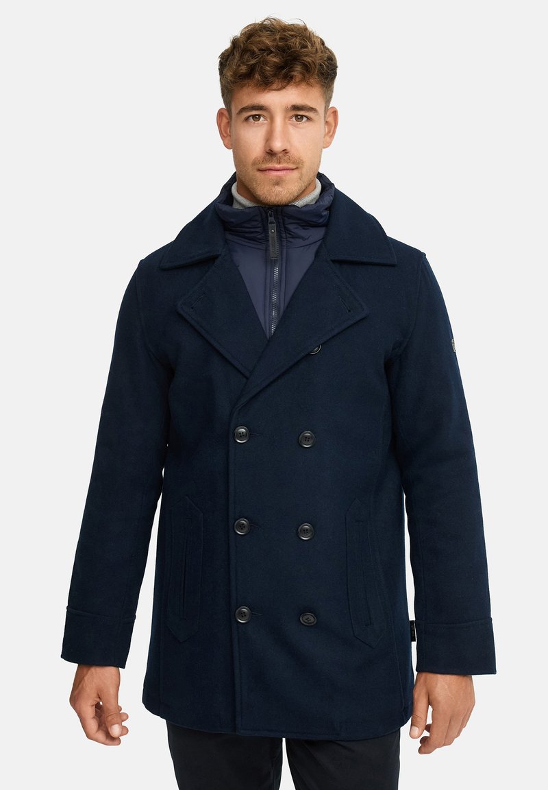 Marineblå uldblandingspeacoat med dobbeltbrystet front, store kraver og to sidelommer. Har sorte knapper og et lynlåslukket indvendigt lag.
