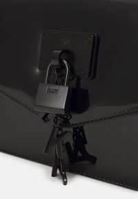 Czarna torebka z lakierowanej skóry ekologicznej z metalowym zamkiem i breloczkiem DKNY, o eleganckim, błyszczącym wykończeniu i stębnowanych detalach.