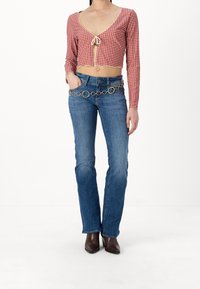 Röd- och vitrutigt kort topp med långa ärmar och knytning vid halsringningen, kombinerad med blå utsvängda jeans och ett guldfärgat cirkelformat kedjebälte.