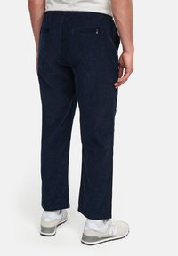 Marineblå corduroy bukser med en afslappet pasform, der har baglommer og kontrasterende sidelapper. Bæres med hvide sneakers.
